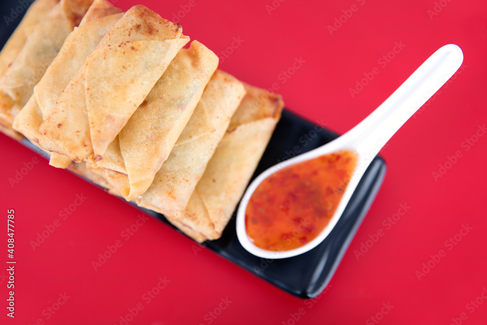 A plate of spring rolls and dip on a red background