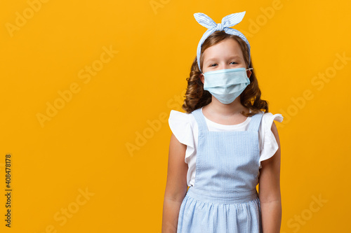 Little girl on a yellow background. Portrait of a child in a protective mask with copy space. © Olga