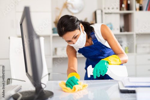 Female cleaner working in protective mask productively on task in office photo