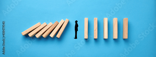Silhouette of a businessman in apathy or inertia against collapsing wooden dominos on blue background. Business crisis and inactivity
