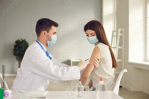 Male nurse or doctor in medical face mask giving injection to female patient during vaccination campaign at health center. Young woman getting flu or Covid-19 vaccine shot at the clinic or hospital
