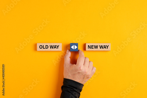 Male hand holds a wooden cube with arrow icon between the options of old way or new way.