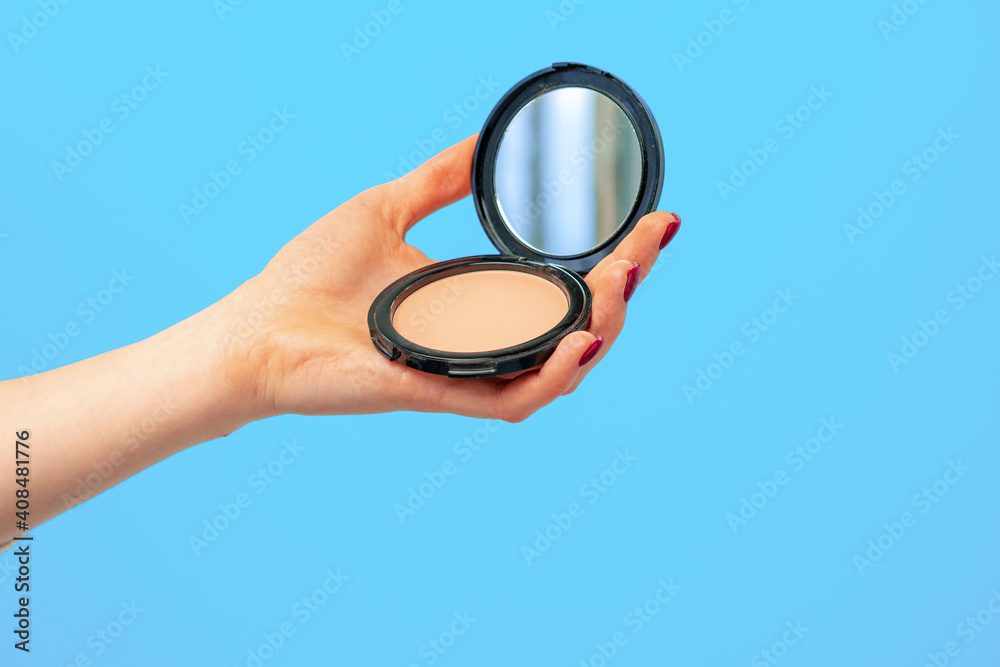 Female hand holding compact powder against blue background Female hand holding compact powder against blue background