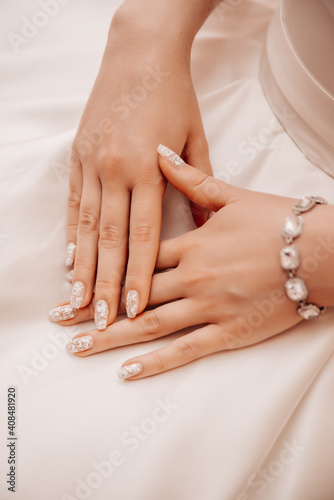 Beautiful well-groomed female hands on the background of a white dress 