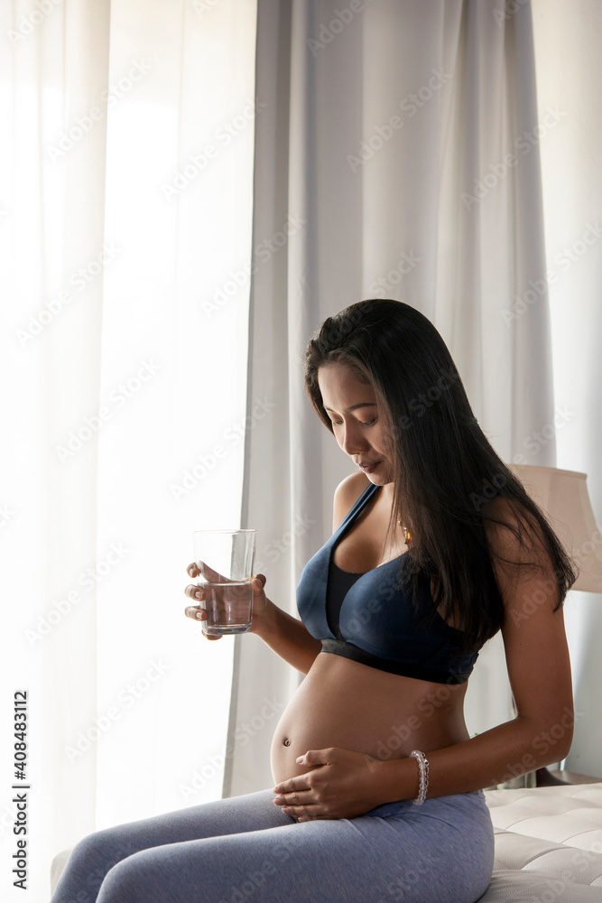 Young beautiful pregnant woman in sportswear Belly while holding a glass of water , Cute pregnant belly. Beautiful pregnant woman Young beautiful pregnant woman in sportswear Belly while holding a glass of water , Cute pregnant belly. Beautiful pregnant woman