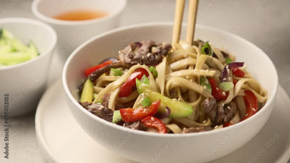 Chopsticks mixed noodles with vegetables and beef in a deep white bowl Chopsticks mixed noodles with vegetables and beef in a deep white bowl