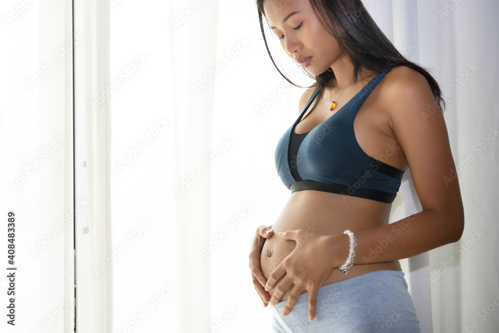 Side view of asian pregnant woman touching her belly at home with copy space for texture Side view of asian pregnant woman touching her belly at home with copy space for texture