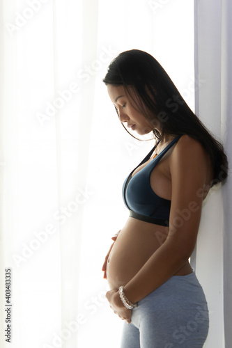 Side view of asian pregnant woman touching her belly at home with copy space for texture