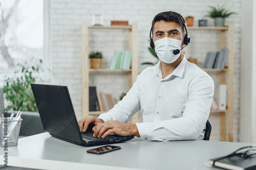 Young businessman sitting at his working desk with medical mask on Young businessman sitting at his working desk with medical mask on