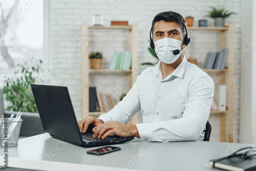 Young businessman sitting at his working desk with medical mask on