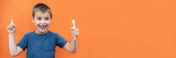 Boy without milk upper tooth in blue t-shirt holds toothbrush in hand on the orange background. Copy space. Banner.