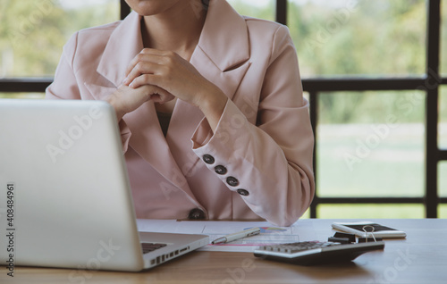 Businesswoman working on laptop in her workstation.Black blank screen smartphone, potted plant, pencil, notes, earphone on wooden desk. Close up
