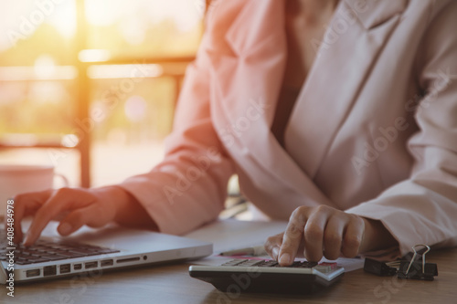 Businesswoman working on laptop in her workstation.Black blank screen smartphone, potted plant, pencil, notes, earphone on wooden desk. Close up
