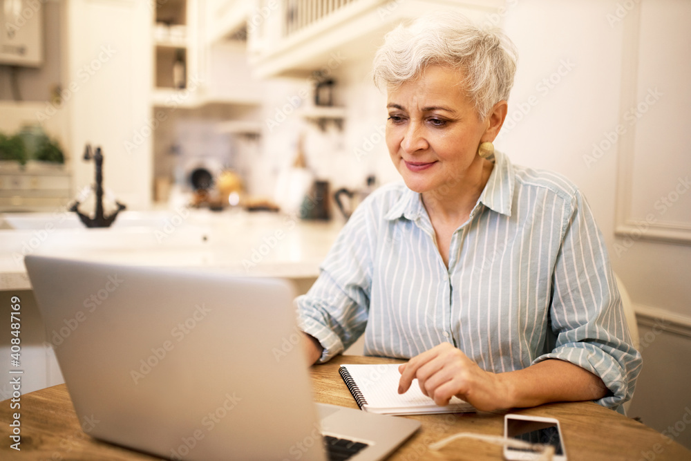 Creative mature female freelancer sitting in front of generic laptop making research, writing new post or article for her online blog on social media. Attractive retired woman using portable computer Creative mature female freelancer sitting in front of generic laptop making research, writing new post or article for her online blog on social media. Attractive retired woman using portable computer