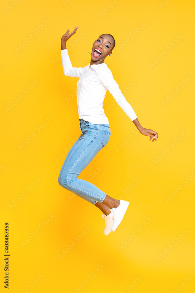 Happy smiling African American woman jumping in yellow isolated studio background