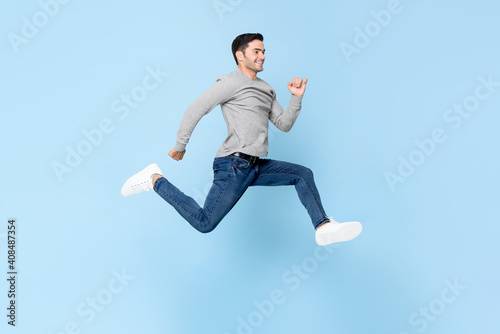 Smiling handsome man jumping in light blue color isolated studio background
