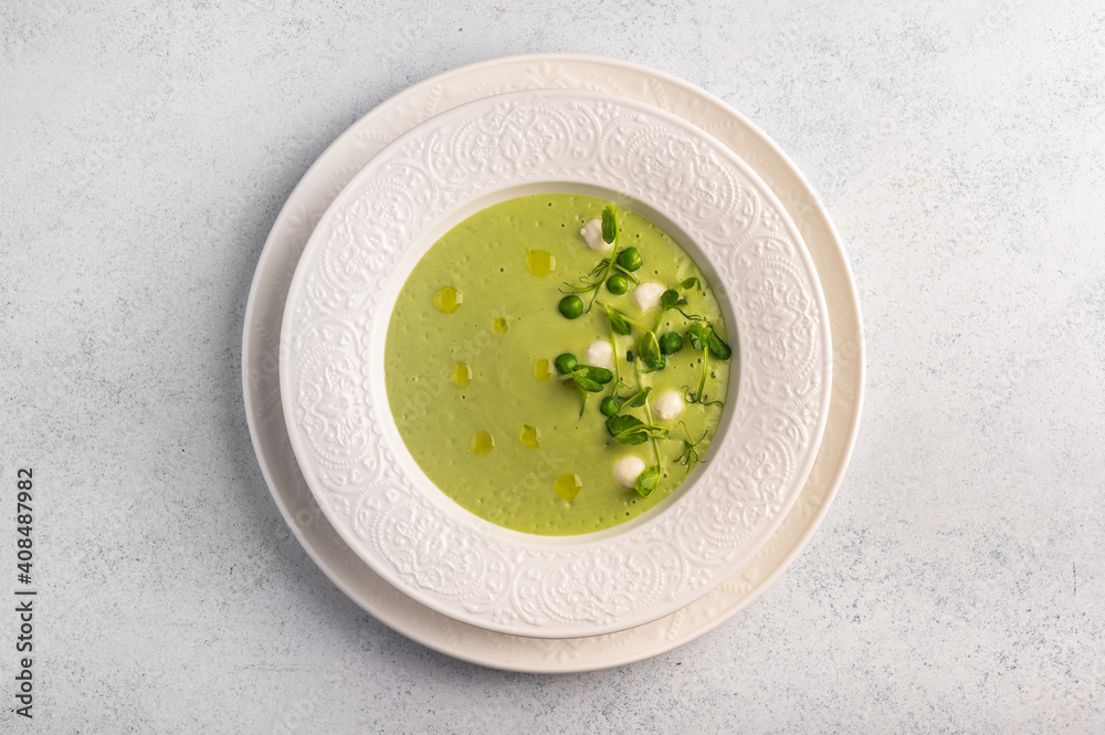 Homemade soup puree of green peas, coconut milk with mini mozzarella cheese in white plate on light background, top view Homemade soup puree of green peas, coconut milk with mini mozzarella cheese in white plate on light background, top view