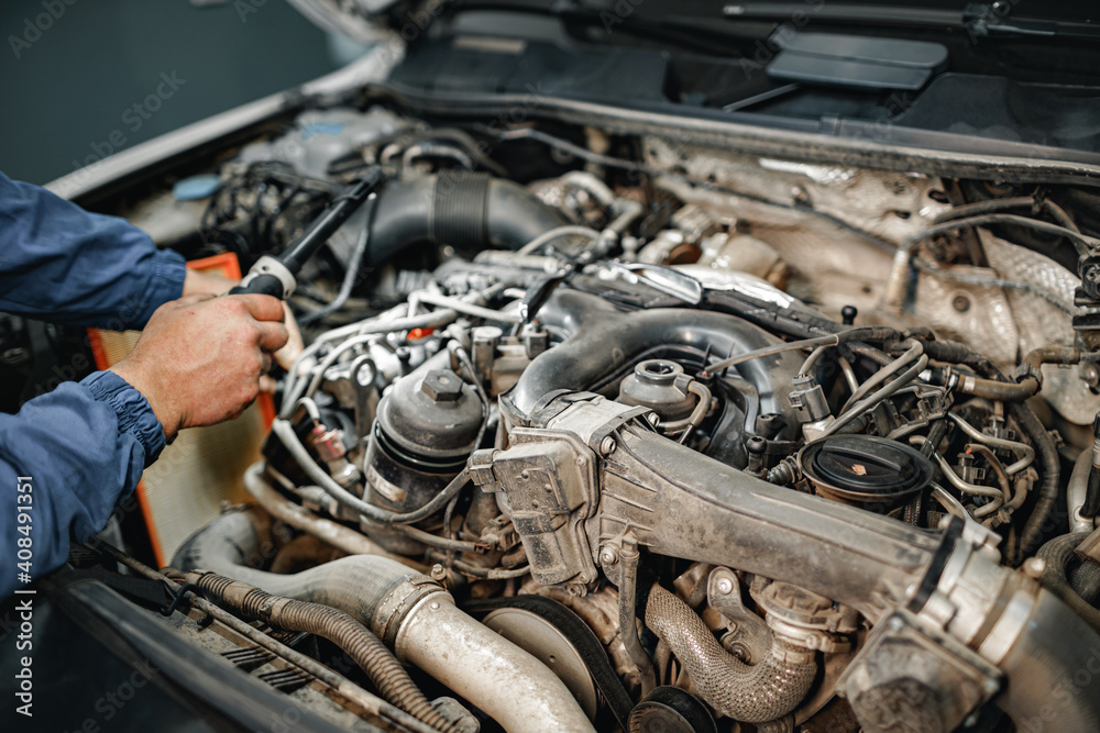 Auto mechanic man checks car engine under the hood Auto mechanic man checks car engine under the hood
