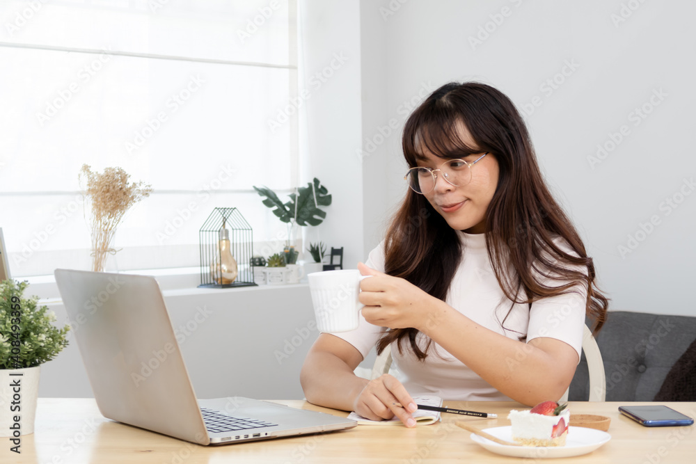 Asian woman raising a coffee cup, interacting using Video Call looking at the laptop computer.