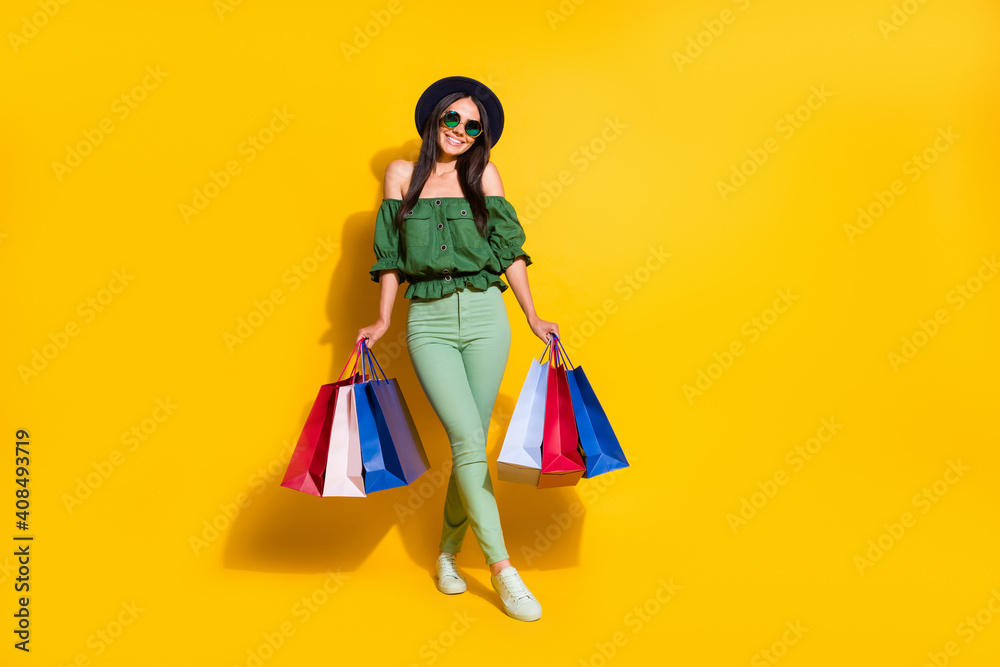 Full length photo portrait of shy girl holding shopping bags in two hands isolated on vivid yellow colored background
