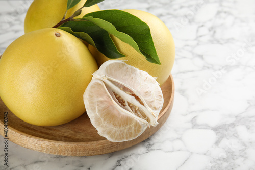 Fresh cut and whole pomelo fruits with leaves on white marble table, closeup. Space for text
