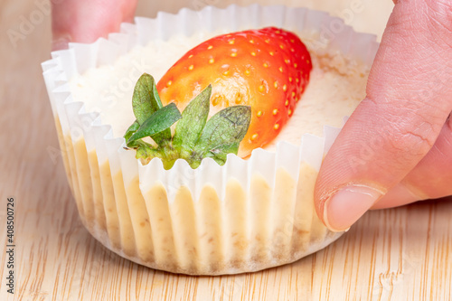 Selective focus closeup of a hand holding a strawberry on a cheesecake on the wooden table photo