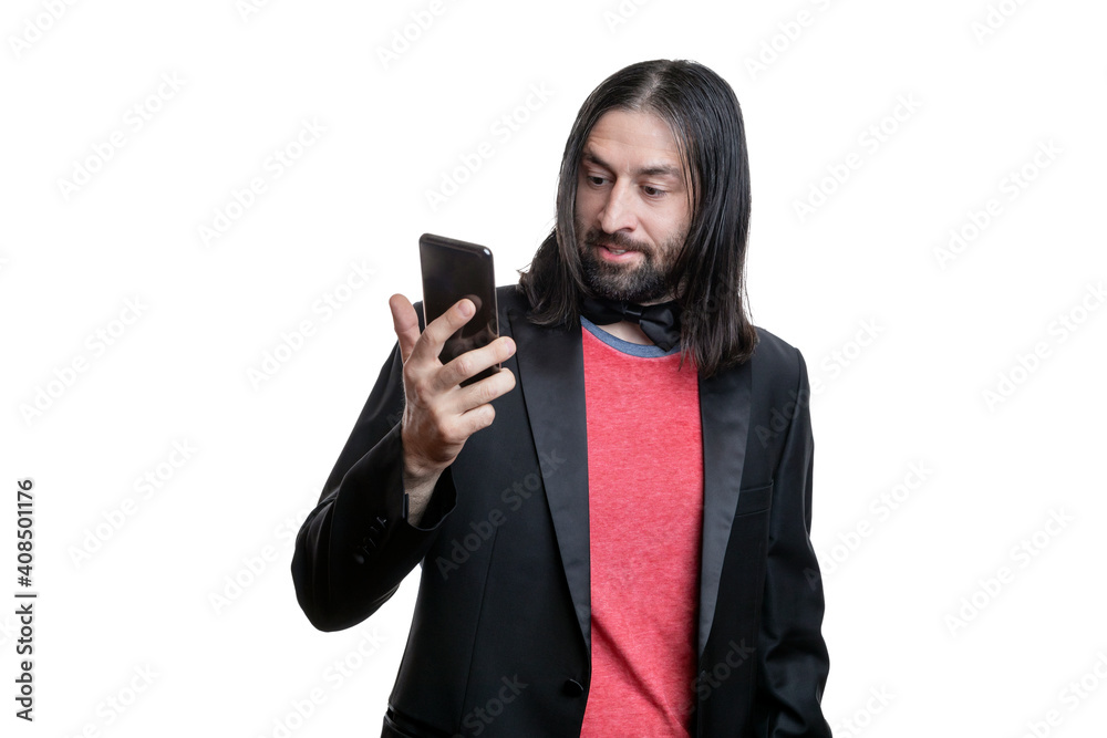Portrait of a young man with long hair and a goatee in a black leather jacket and red T-shirt with a phone in his hands isolated on a white background. The concept of human emotions. Portrait of a young man with long hair and a goatee in a black leather jacket and red T-shirt with a phone in his hands isolated on a white background. The concept of human emotions.
