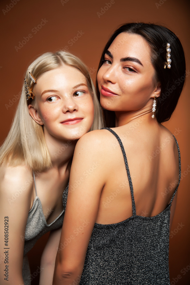 two pretty diverse girls happy posing together: blond and brunette on brown background, lifestyle people concept two pretty diverse girls happy posing together: blond and brunette on brown background, lifestyle people concept