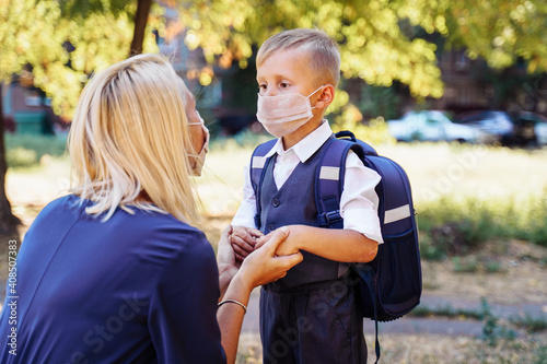 Mom is ready to send her little son to first grade. Gently holds the boy's hands. They are wearing protective medical masks. New requirements for training during the quarantine period Coronavirus-19