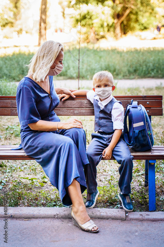 Mom and her son, a schoolboy, are sitting on a bench in the yard. They put on medical masks to protect themselves from the coronavirus. Important methods of protection against Covid-19
