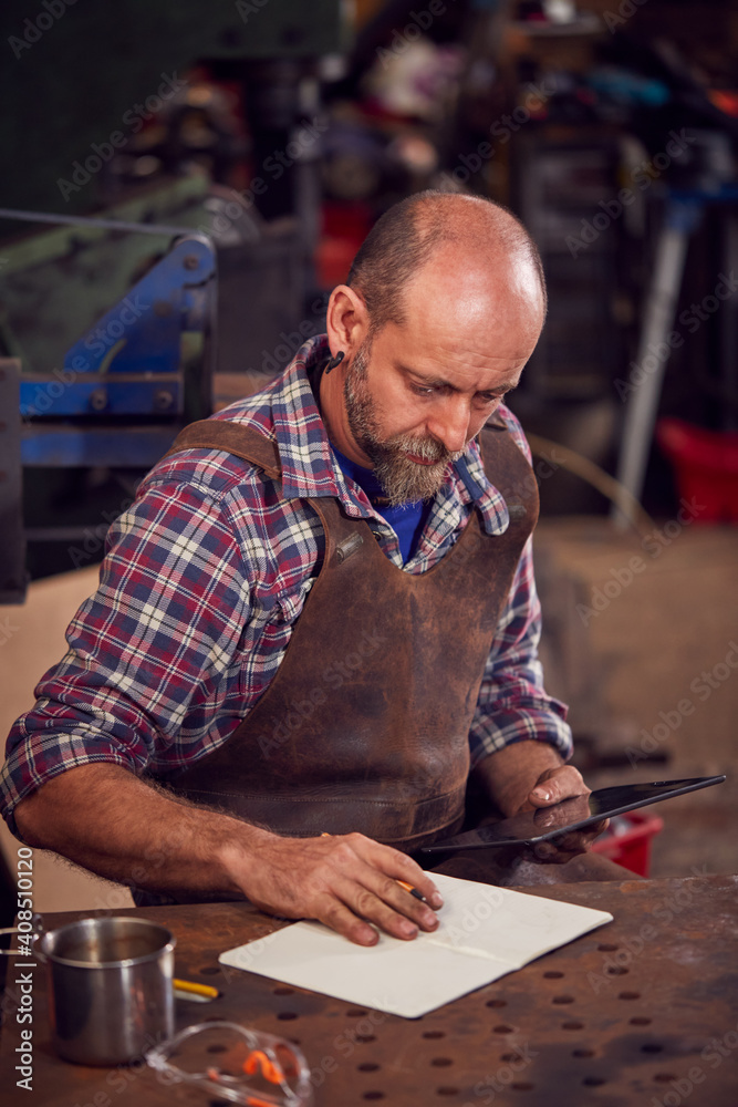 Mature Male Blacksmith Wearing Apron Working On Design In Forge Mature Male Blacksmith Wearing Apron Working On Design In Forge
