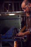Male Blacksmith Shaping Metalwork On Belt Sander With Sparks