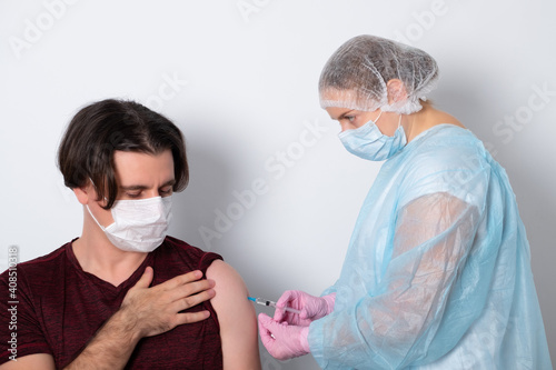 Medicine, vaccination and healthcare concept - doctor wearing face protective medical mask for protection from virus disease with syringe doing injection of vaccine to male patient.