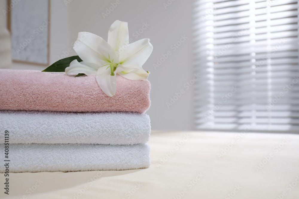 Stack of clean towels and flower on bed indoors, closeup. Space for text Stack of clean towels and flower on bed indoors, closeup. Space for text
