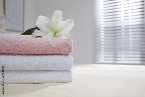 Stack of clean towels and flower on bed indoors, closeup. Space for text