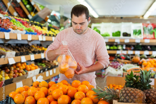Young man customer choosing fresh oranges on the supermarket
