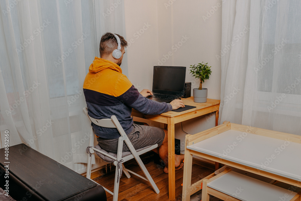 Young man playing computer games in white headphones. Gamer at home. Man working on computer at home.