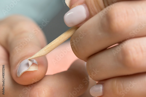 Remove the gel polish with a wooden stick. Woman is removing gel polish shellac from nails using pusher, manicure at home. Removing gel Polish from nails, hands closeup. Manicure. Beauty, skin care.