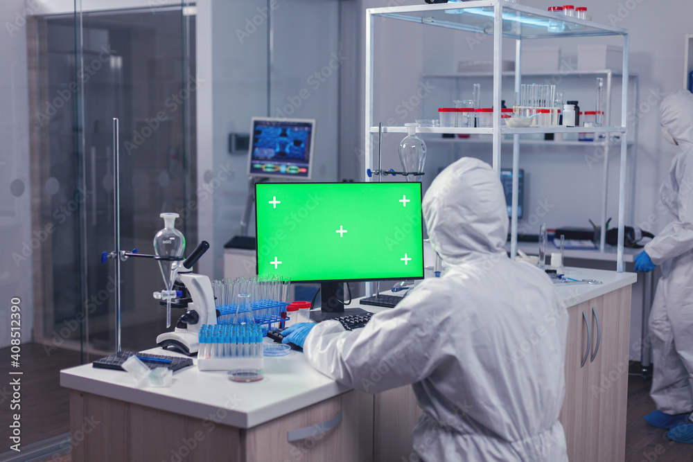 Scientist sitting at his workplace using computer with green screen. Team of microbiologists doing vaccine research writing on device with chroma key, isolated, mockup display. Scientist sitting at his workplace using computer with green screen. Team of microbiologists doing vaccine research writing on device with chroma key, isolated, mockup display.