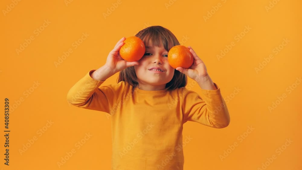 The child opens and closes his eyes with oranges. A little boy plays with fruit on a yellow background. The child opens and closes his eyes with oranges. A little boy plays with fruit on a yellow background.