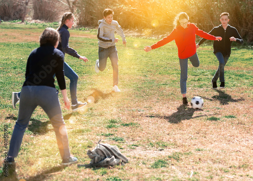 Company of glad teenagers playing football in park