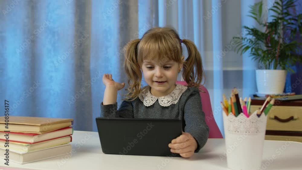 Child schoolgirl learns lessons with teacher being at home sitting at table using digital tablet computer. Portrait of a kid pupil girl distance education. Studying on coronavirus quarantine lockdown Child schoolgirl learns lessons with teacher being at home sitting at table using digital tablet computer. Portrait of a kid pupil girl distance education. Studying on coronavirus quarantine lockdown