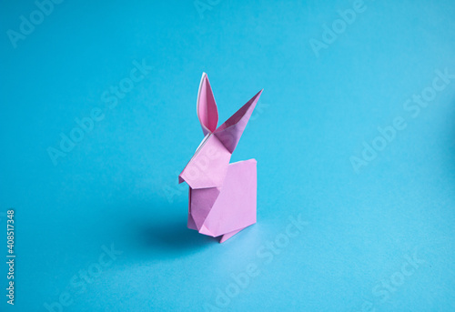 Step-by-step instructions for creating  origami bunny out of colored paper on  blue background, for  decorative Easter party decoration or for small Easter gifts.