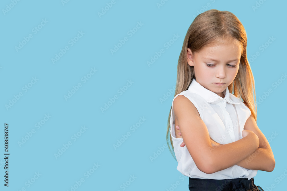 Pensive kid. Hurt feelings. School bullying. Portrait of troubled thoughtful sad little girl in formal outfit standing with folded arms looking down isolated on blue copy space background. Pensive kid. Hurt feelings. School bullying. Portrait of troubled thoughtful sad little girl in formal outfit standing with folded arms looking down isolated on blue copy space background.