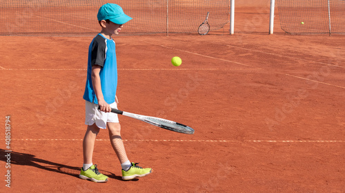 Child tennis player plays with ball and racket on red clay court. Childrens sports and physical activity concept. Kids fun sport game. Background, copy space © Elena