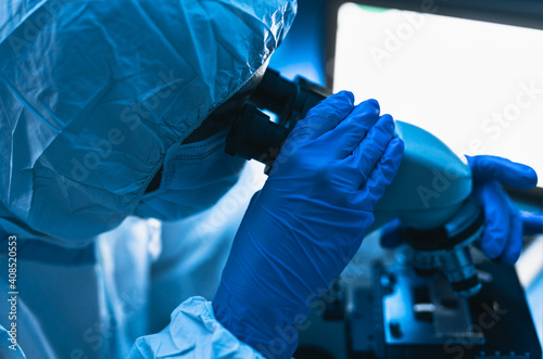 Young scientist working in laboratory examining coronavirus through microscope - Science and technology concept