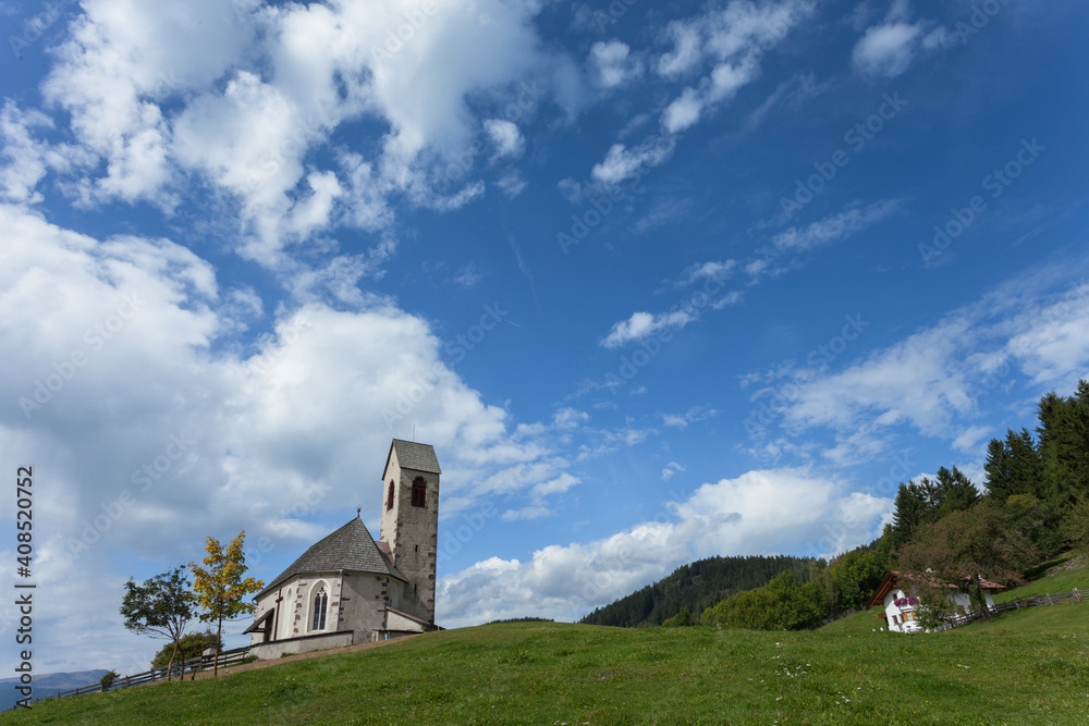 St. Giacomo little church among a wide green meadow in St. Giacomo town , Val di Funes