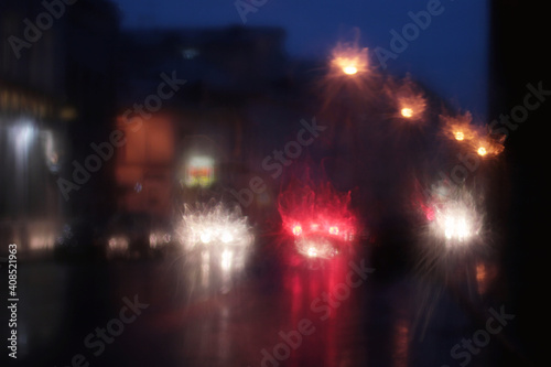 Rainy window  bad weather in the city. Defocused city road with illuminating car moving slowly and look like horror masks