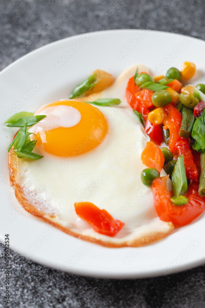 Fried eggs and vegetables in a white plate on a gray concrete stone table for breakfast, close up Fried eggs and vegetables in a white plate on a gray concrete stone table for breakfast, close up