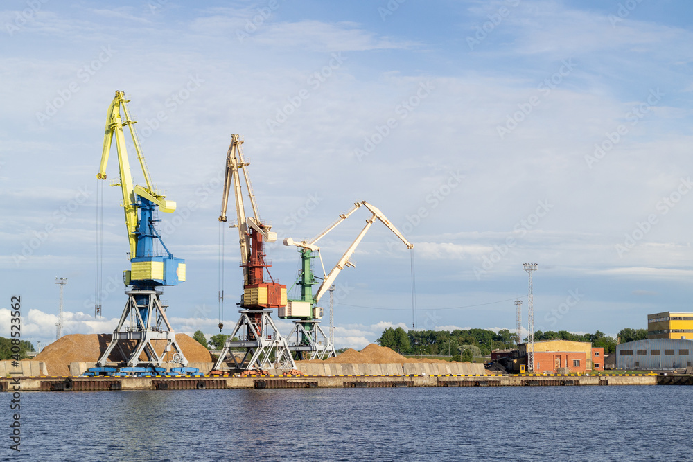 Storage, port crane, industrial scene. Cargo cranes in terminal in river ship port in Ventspils, Latvia, Baltic sea. Shipping import or export, logistic. Venta river.